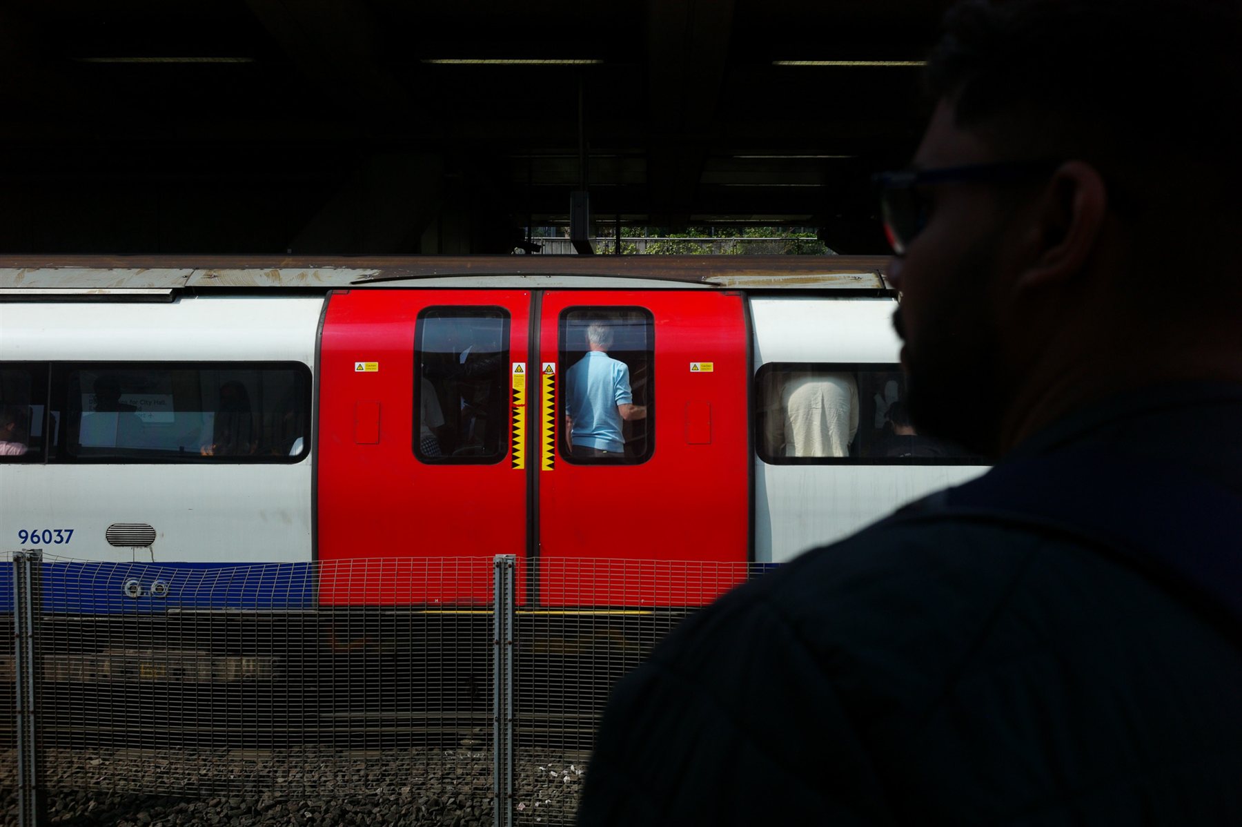 A red Tube train passing behind a silhouetted man on the platform