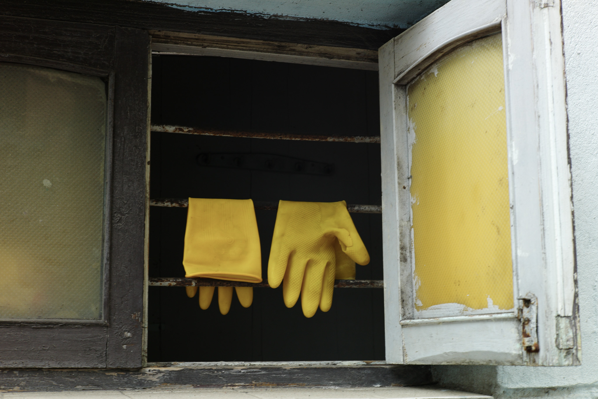 Yellow rubber gloves hanging in an open window, with no hands in them