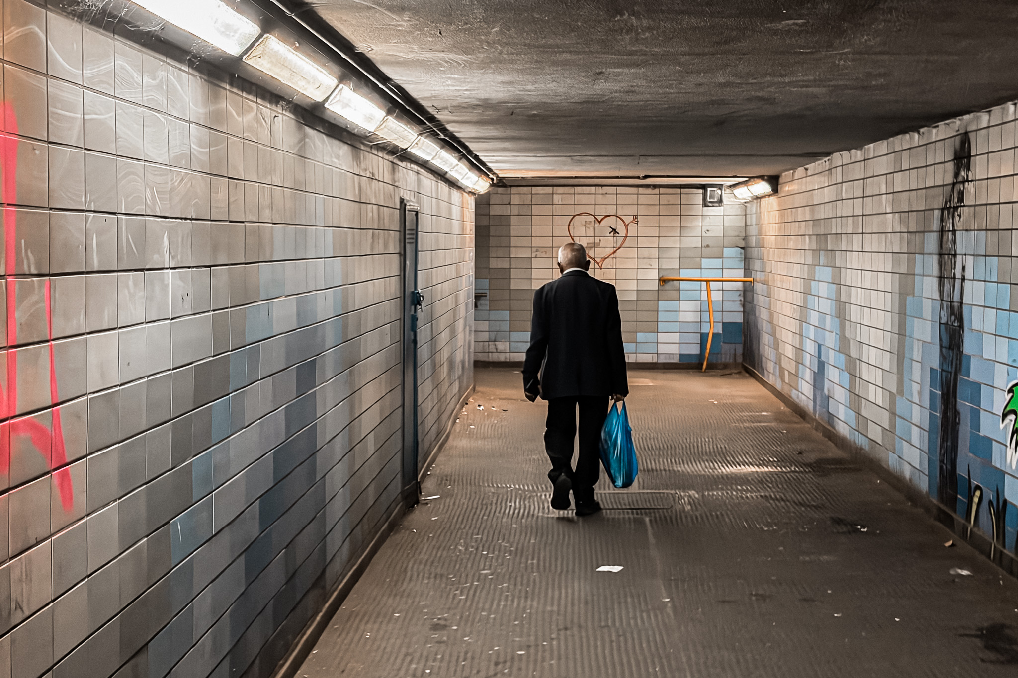 A man walking away down a tiled underpass, a painted heart on the wall ahead