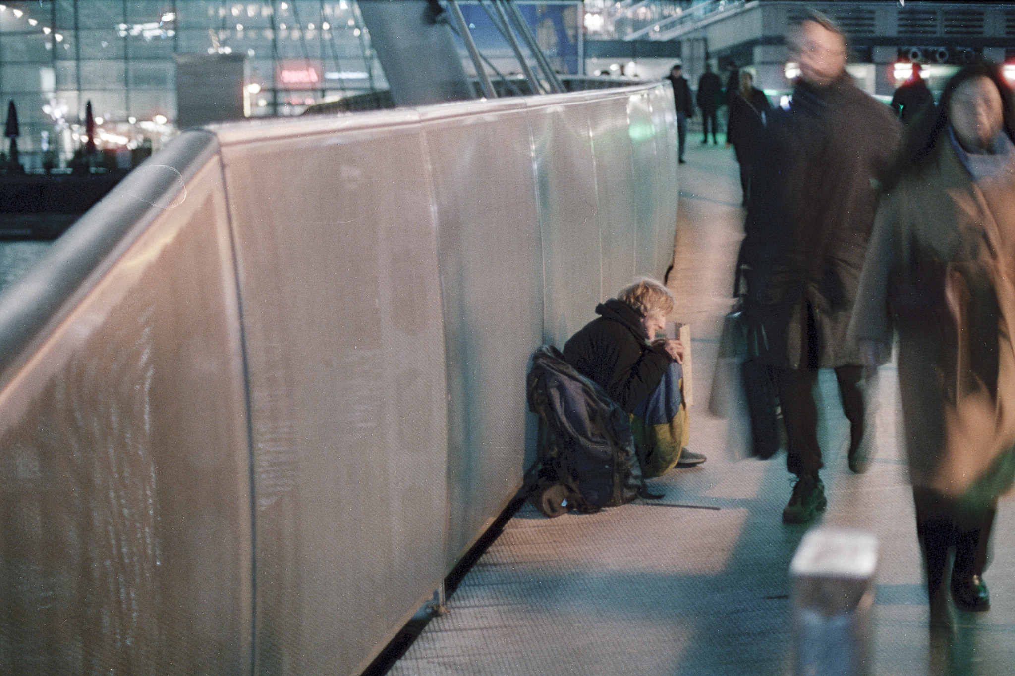 A person sitting against a barrier while commuters pass in motion blur